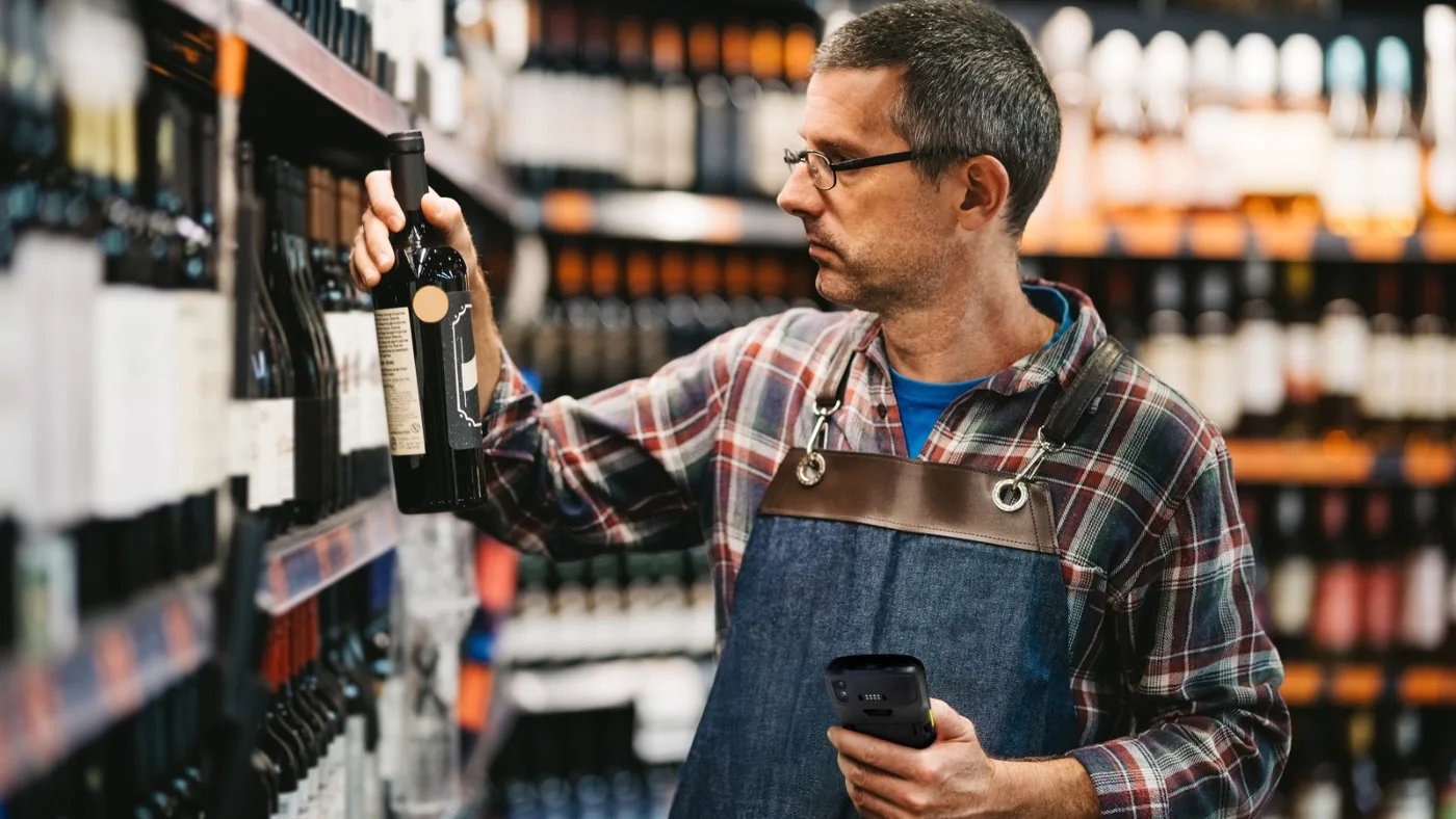 Store employee checking a wine bottle on the shelf with a Zebra handheld mobile computer